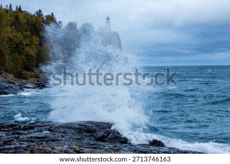Split Rock lighthouse in Minnesota under grey sky.  Large rock bluff with blue and green water splash in foreground.  Motion blur action water against wet rocks.  