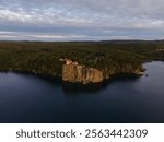 Split Rock Lighthouse sits atop a dramatic cliff, illuminated by golden light, surrounded by lush forest and overlooking a calm coastline