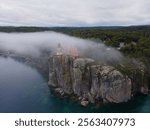 Split Rock Lighthouse stands on a misty cliff, surrounded by dense forest and a dramatic coastal view 