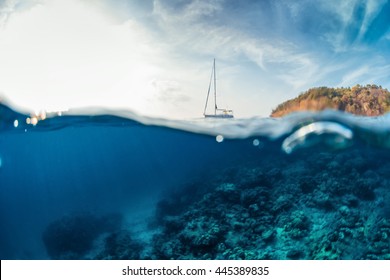 Split shot with hilly tropical terrain on the surface and reef underwater