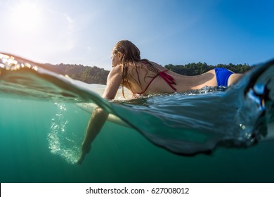 Split shot with underwater view of the woman surfer paddling the board