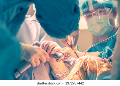 Split Toning Picture Of Team Of Doctor During Perform Total Knee Replacement Surgery In Operating Room. Selective Focus At Oscillating Saw That Cutting On The Bone Intention To Motion Blurred.