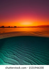 Split view with bright sunset and underwater sandy bottom.