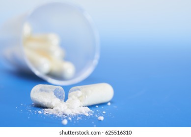 Split-open transparent capsule with white powder on blue gradient background, text space