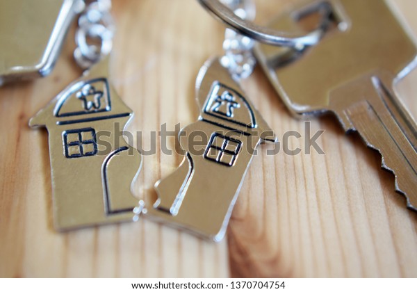 Splitted\
or broken  pendant of key ring in shape of house divided in two\
parts on wooden background, closeup view. Dividing house when\
divorce, division of property and real\
estate.\
