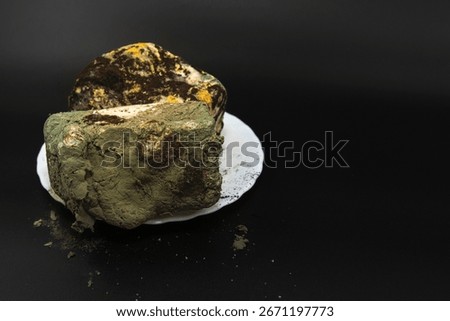 Spoiled bread completely covered with green black and yellow mold fungus on plate over dark background concept of food waste unhealthy product and toxic contamination