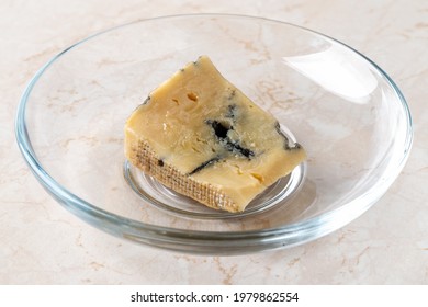 Spoiled Dried Cheese Scrap. Small Piece Of Dor Blue Cheese Has Dried On A Plate On The Table. Food Spoiled Due To Storage Outside The Fridge. Biodegradable Food Waste And Organic Leftovers. Close-up.