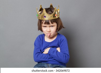 spoiled kid concept - cheeky preschool child with golden crown on head folding arms and sticking out tongue for disrespectful mollycoddled little king or queen metaphor,studio shot