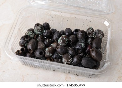 Spoiled Olives With White Green Mold In A Plastic Food Container On A Kitchen Table. Mold Fungus On Stale Olives. Food Forgotten In The Fridge. Front View.