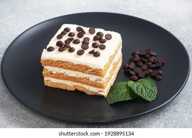 Schwammkuchen mit Buttercreme und Schokoladenstücken minzen auf einem schwarzen Teller. Dessert zum Feiern oder Geburtstagsfest
