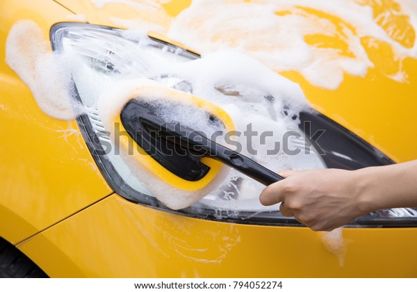 sponge washer\
cleaning headlights of a yellow\
car