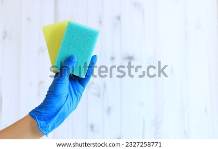 Sponges for washing dishes in a female hand on a light wood background. A hand in a latex glove holds two sponges for wet cleaning. Professional cleaning. copy space