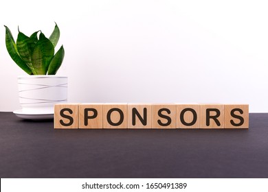 SPONSORS word concept written on wooden blocks, cubes on a dark table with a flower and a light background