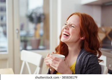 Spontaneous attractive young redhead woman enjoying a good laugh over a morning cup of coffee at home in the apartment - Shutterstock ID 385838179