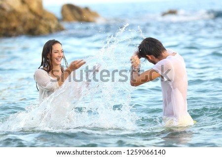 Spontaneous couple joking throwing water bathing in the sea on the beach