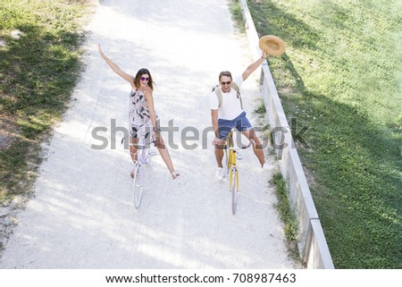 A spontaneous romantic tourist couple riding a bike on a cycle lane. Fashion blonde boyfriend and girlfriend walking on the park with vintage bike.. concept love