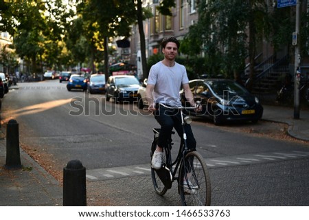 Spontaneous and smiling Dutch male student riding on his bicycle through an old and cosy street in Amsterdam, the Netherlands.