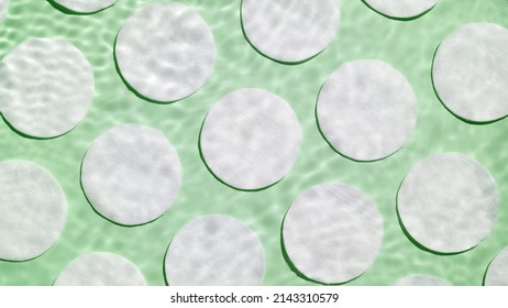 Spontanous water ripples over cotton pads arranged in rows on green background | Background shot for cleanser or micellar water beauty product