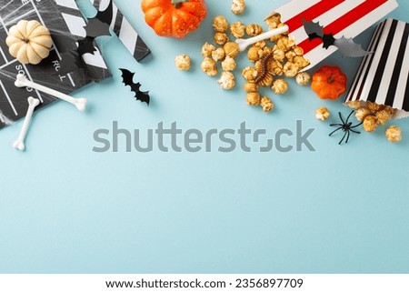 Spooky Cinema Setup: Top view of themed decorations featuring bone-adorned popcorn boxes and eerie insects. Pumpkins, clapperboard, chilling props on pastel blue backdrop with ad-friendly empty space