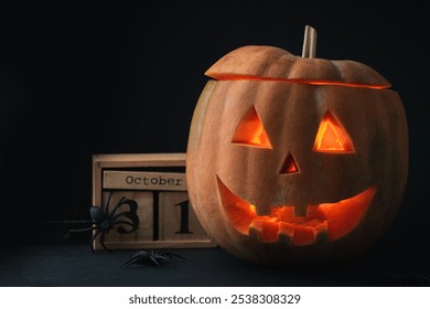 Spooky creepy glowing carved halloween pumpkin on the black background. Jack-o-lantern next to wooden block calendar with the date October 31 surrounded with spiders. Happy Halloween background - Powered by Shutterstock