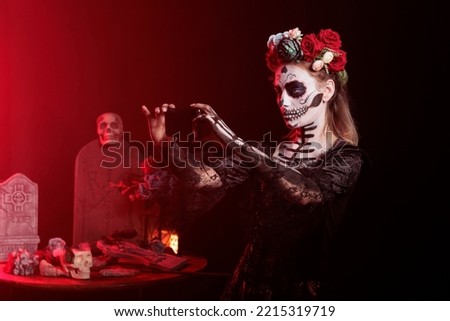 Spooky goddess of death taking photos on smartphone, capturing horror image on mobile phone camera. Woman with make up and mexican halloween costume standing in studio, holy dios de los muertos.
