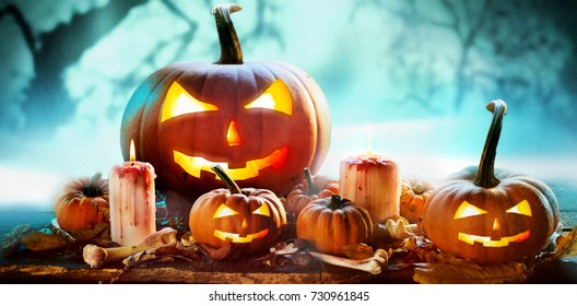 Spooky Halloween banner in a misty forest with an arrangement of glowing evil jack-o-lantern pumpkins and burning candles with dried leaves, bones and copy space