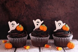 Spooky Halloween Chocolate Cupcakes With Ghosts And Pumpkins In A Row Against A Dark Wood Background