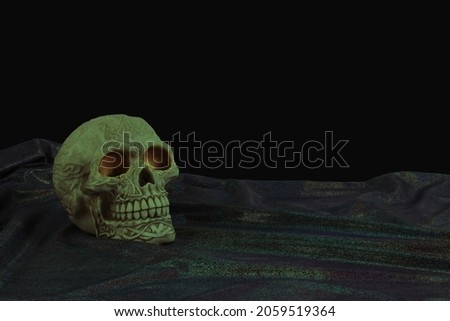 Spooky Halloween scary skull dark message background - dark shiny cloth foreground and black background with an orange eyed Celtic skull on left with space for copy