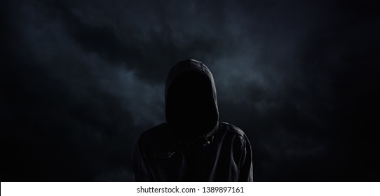 Spooky Hooded Person With Obscured Face Against The Dark Dramatic Sky