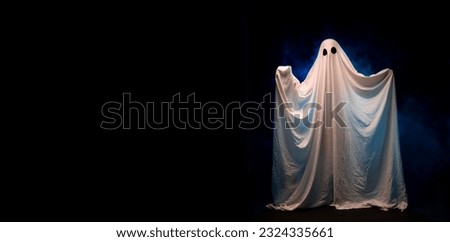 A spooky white ghost covered by a sheet with black eyes over dark background in fog. Banner. Copy space