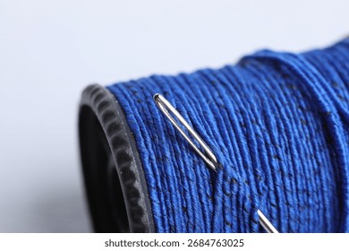 Spool of blue thread with needle on grey background, closeup