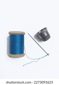 A spool of blue thread, thimble and needle