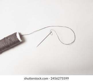 
A spool of brown sewing thread with a needle next to it isolated on a white background - Powered by Shutterstock