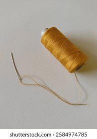 A spool of gold thread with a needle and a threaded end