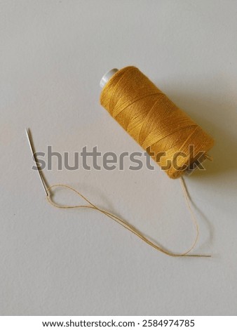 A spool of gold thread with a needle and a threaded end