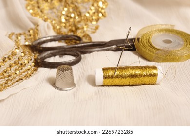 Spool of Gold Thread and Scissors With Thimble on Off White Fabric With Gold Sequins