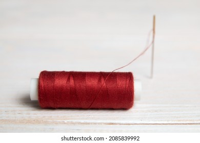 A spool of red thread and a needle on a light background. 