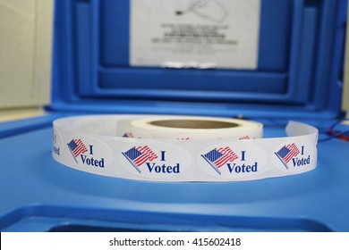 A spool of Red white and blue "I voted" stickers with American flag are on a blue voting booth platform. 