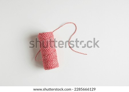 A spool of red and white cotton thread on a white table, isolated. Red and white string on a white background. Wrapping string for presents