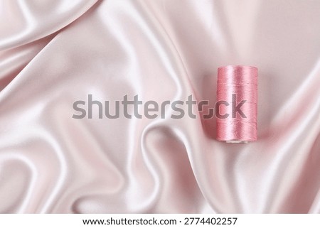 Spool of sewing thread on beige silk fabric, top view. Space for text