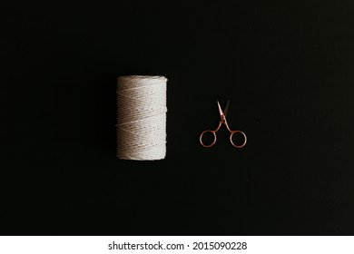 A Spool Of White Cotton Rope, And A Rose Gold Scissors On Black Background.