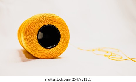A spool of yellow nylon knitting yarn on a white fabric background. The hole of the spool is photographed from below the spool.