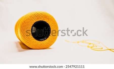 A spool of yellow nylon knitting yarn on a white fabric background. The hole of the spool is photographed from below the spool.