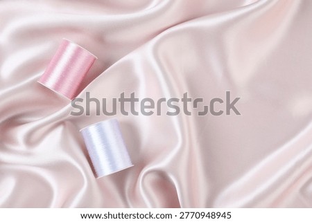 Spools of sewing threads on beige silk fabric, top view. Space for text