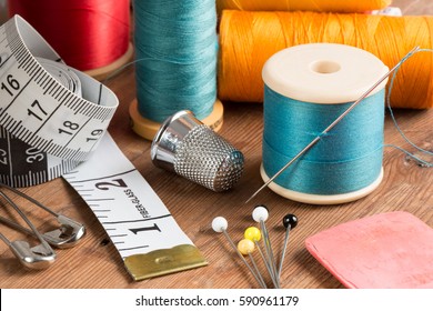 Spools of thread and basic sewing tools including pins, needle, a thimble, and tape measure on a wooden tabletop