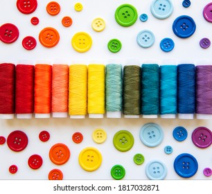 Spools of thread and buttons on the colors of the rainbow on a white background, flat lay