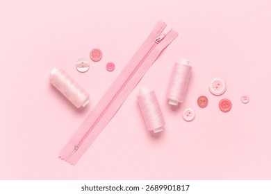 Spools of thread with buttons and zipper on pink background