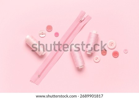 Spools of thread with buttons and zipper on pink background