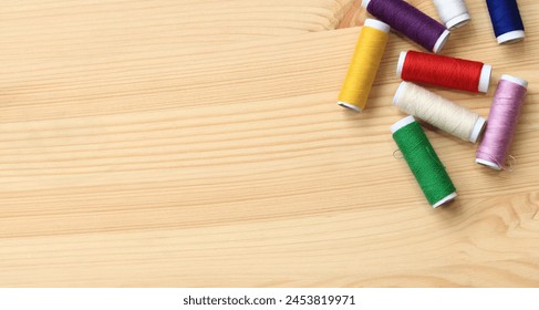 Spools of thread of different colors, top view. Set of various colorful sewing threads on a wooden table, close-up. Sewing