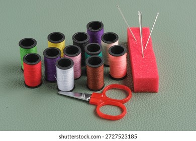 Spools of thread, scissors and red foam needle stand on green leather background